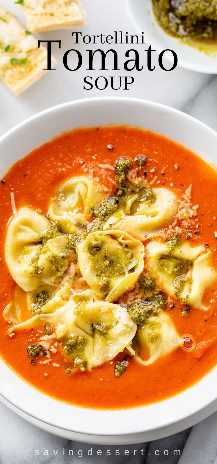 A closeup of a bowl of tortellini tomato soup with pesto and grated Parmesan