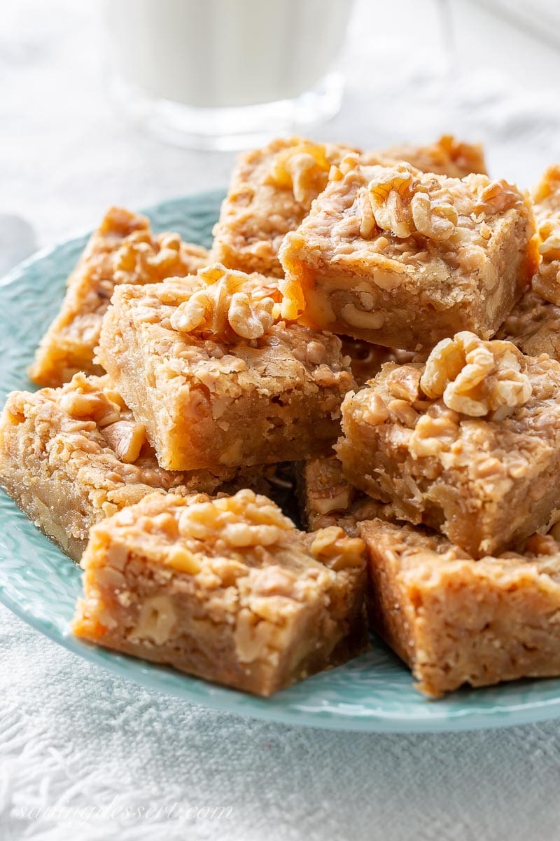 A stack of walnut toffee bars on a plate with a glass of milk