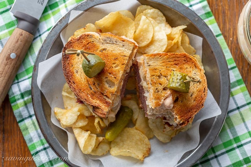 A toasted and sliced Reuben sandwich with chips and pickles