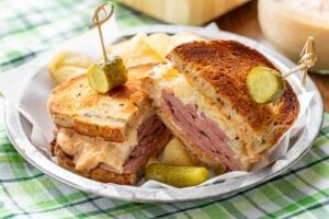 A sliced corned beef sandwich served with chips and a pickle