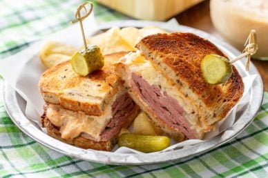 A sliced corned beef sandwich served with chips and a pickle