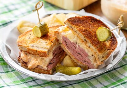 A sliced corned beef sandwich served with chips and a pickle