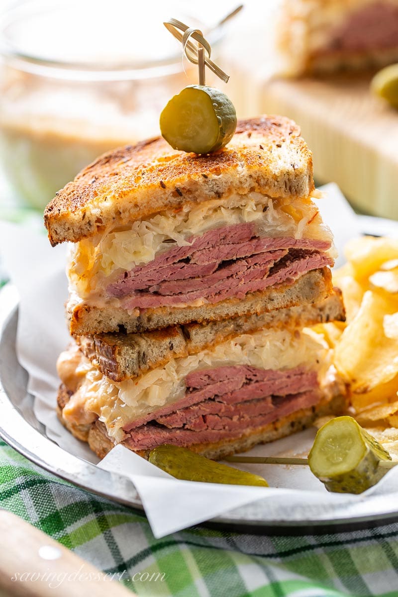 A stacked Reuben sandwich with pickles and served with chips