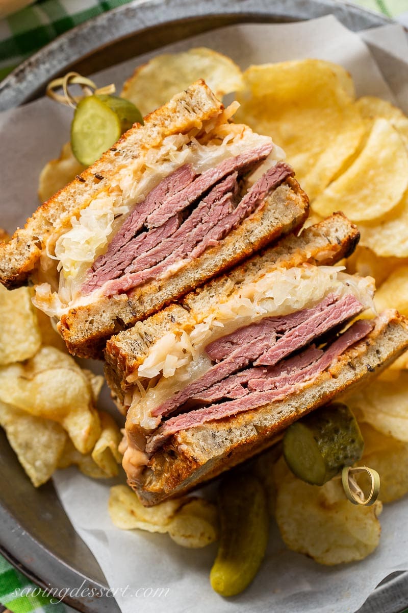 A sliced Reuben sandwich served with chips and pickles