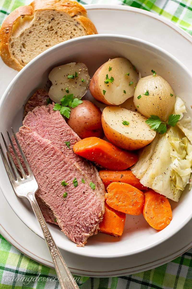 A bowl of corned beef and cabbage served with rye bread and vegetables on the side