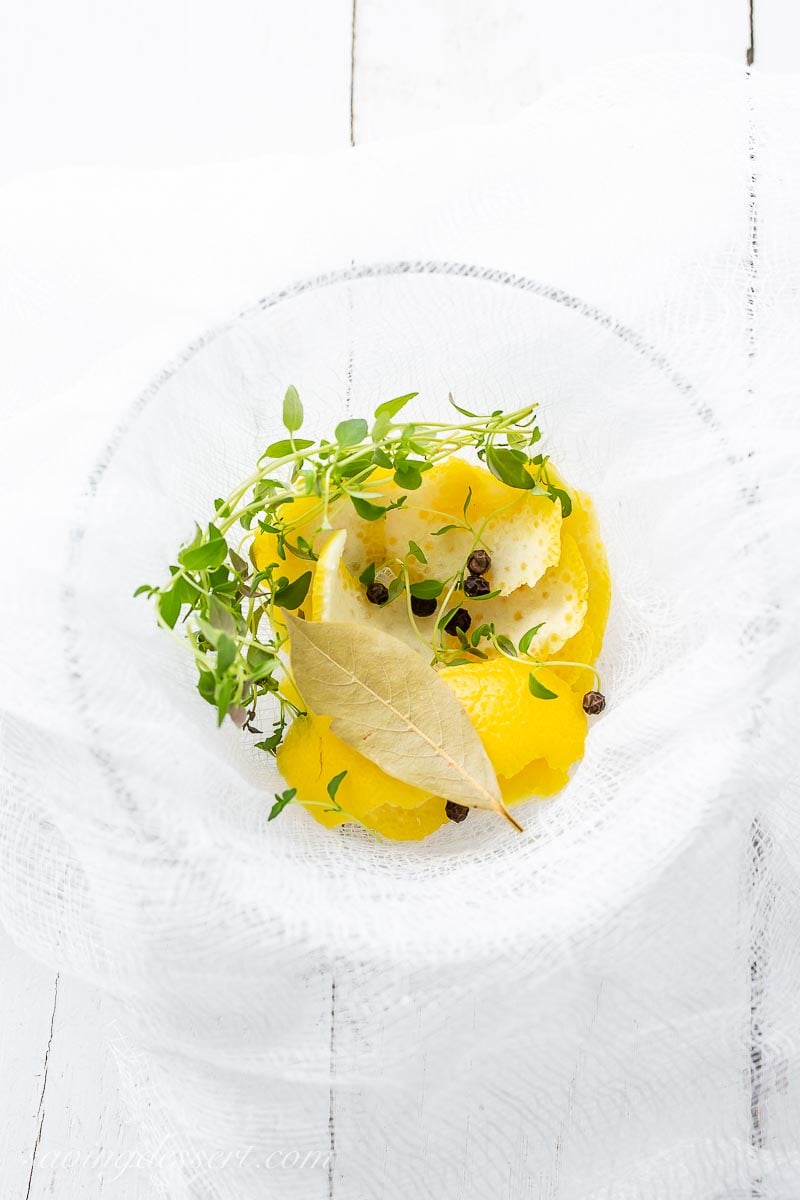 A small bowl with a cheesecloth bundle of thyme, lemon, peppercorns and a bay leaf