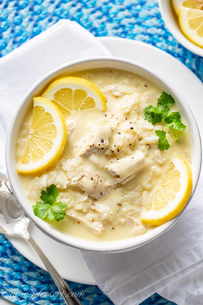 A bowl of Greek chicken and rice soup topped with sliced lemons and fresh ground black pepper