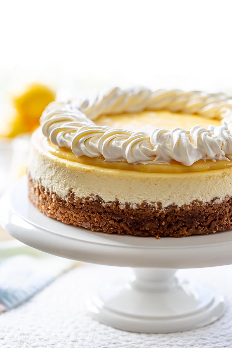 A lemon cheesecake with a graham cracker crust on a cake stand