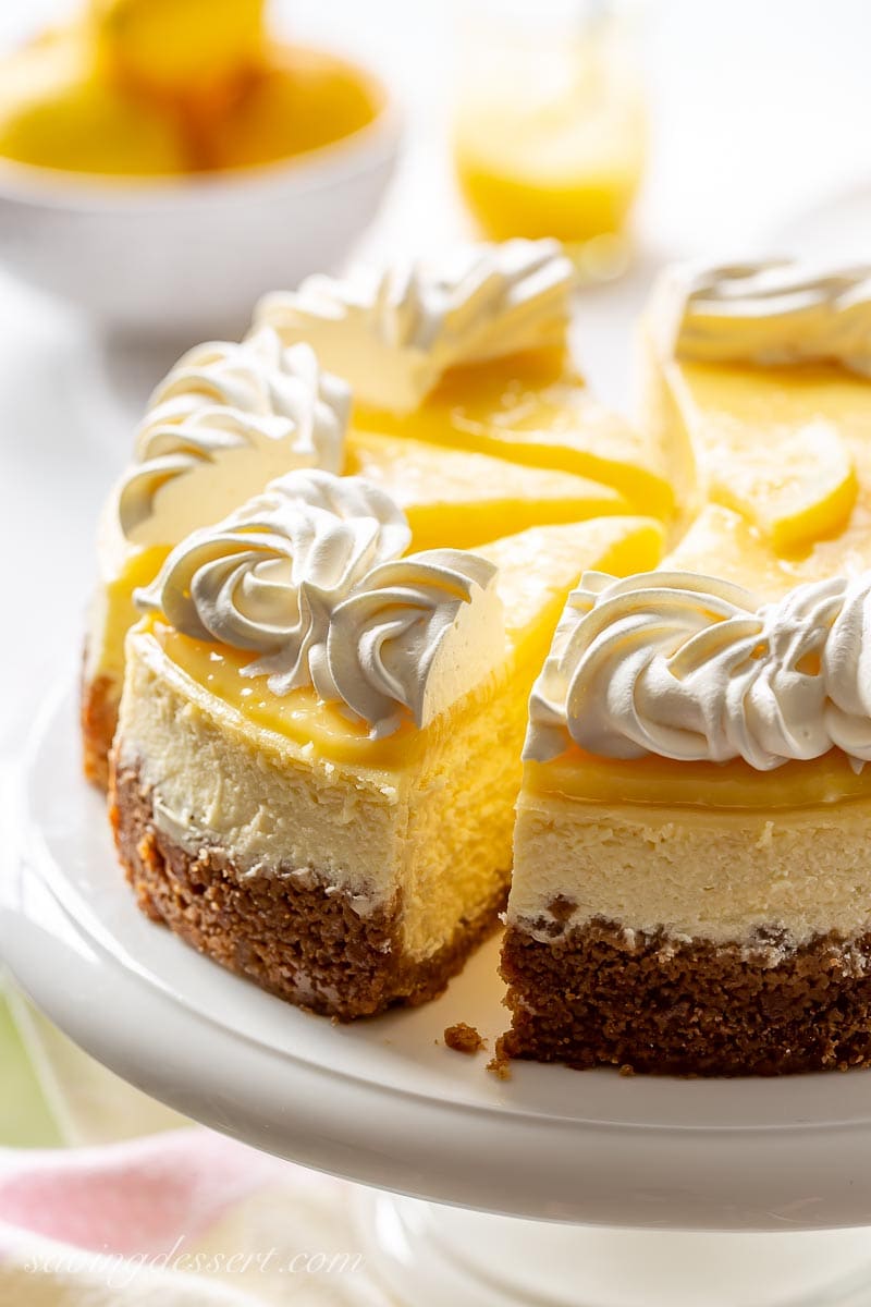 A sliced lemon cheesecake topped with whipped cream on a cake stand