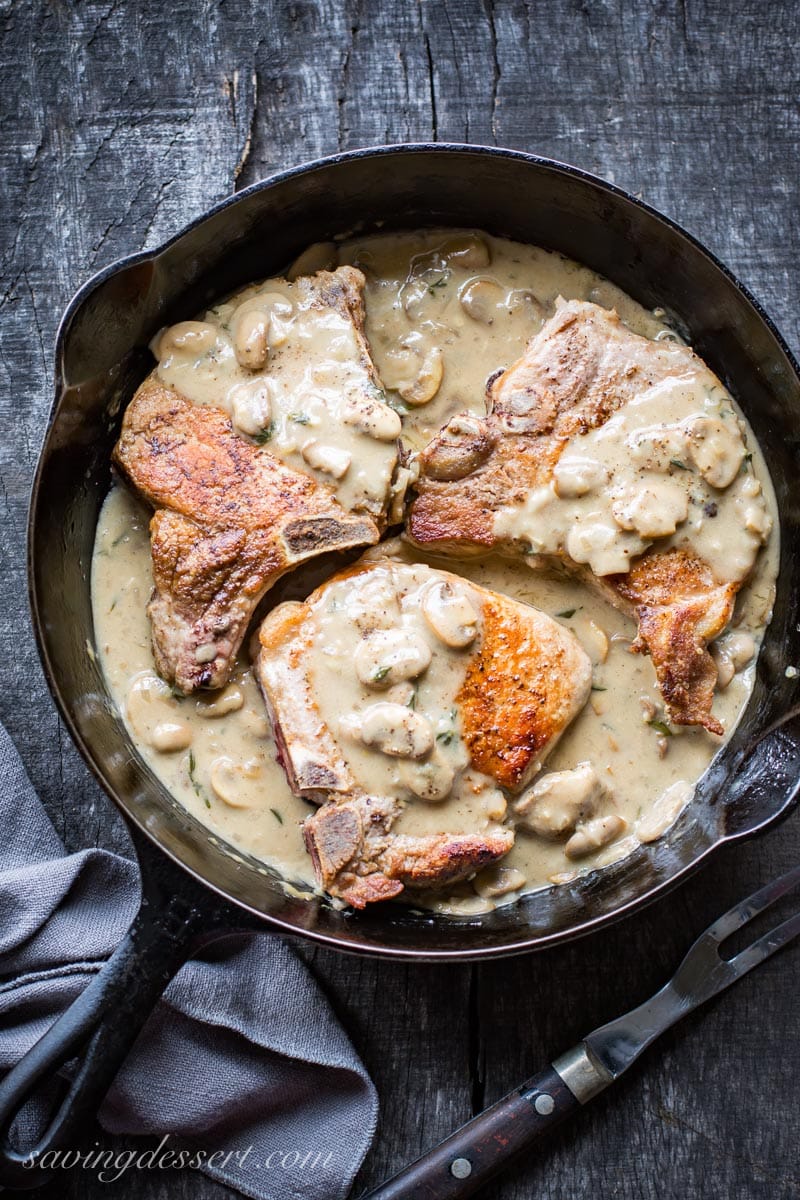 A cast iron skillet filled with bone-in pork chops covered in a mushroom wine pan sauce