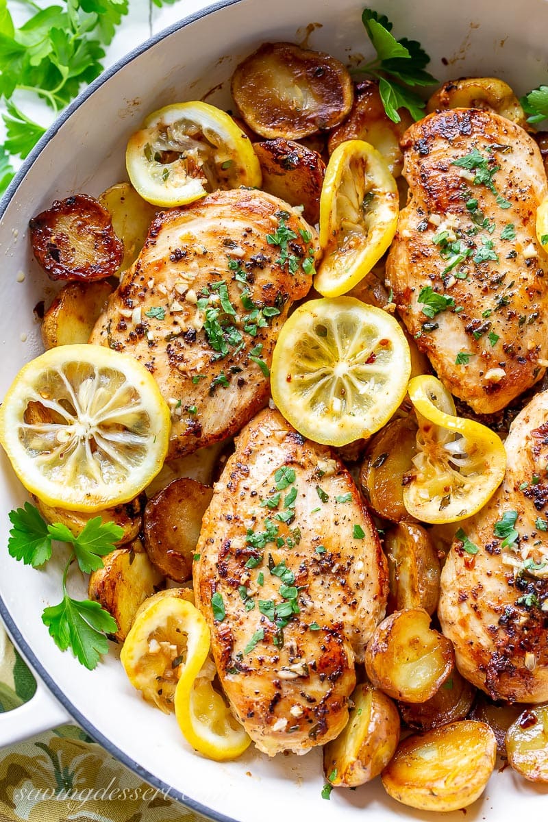 A skillet filled with chicken breasts, roasted potatoes and lemon slices