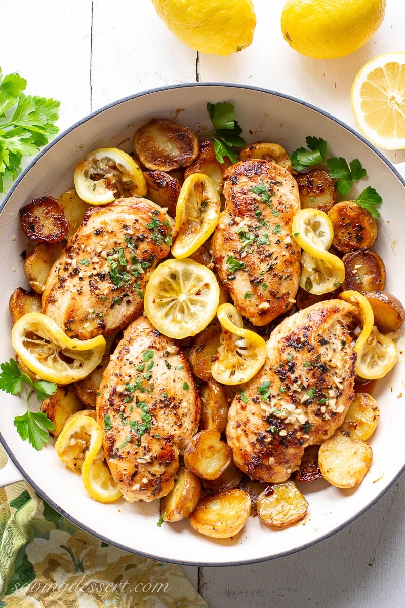 A skillet with chicken breasts, lemon slices and potatoes