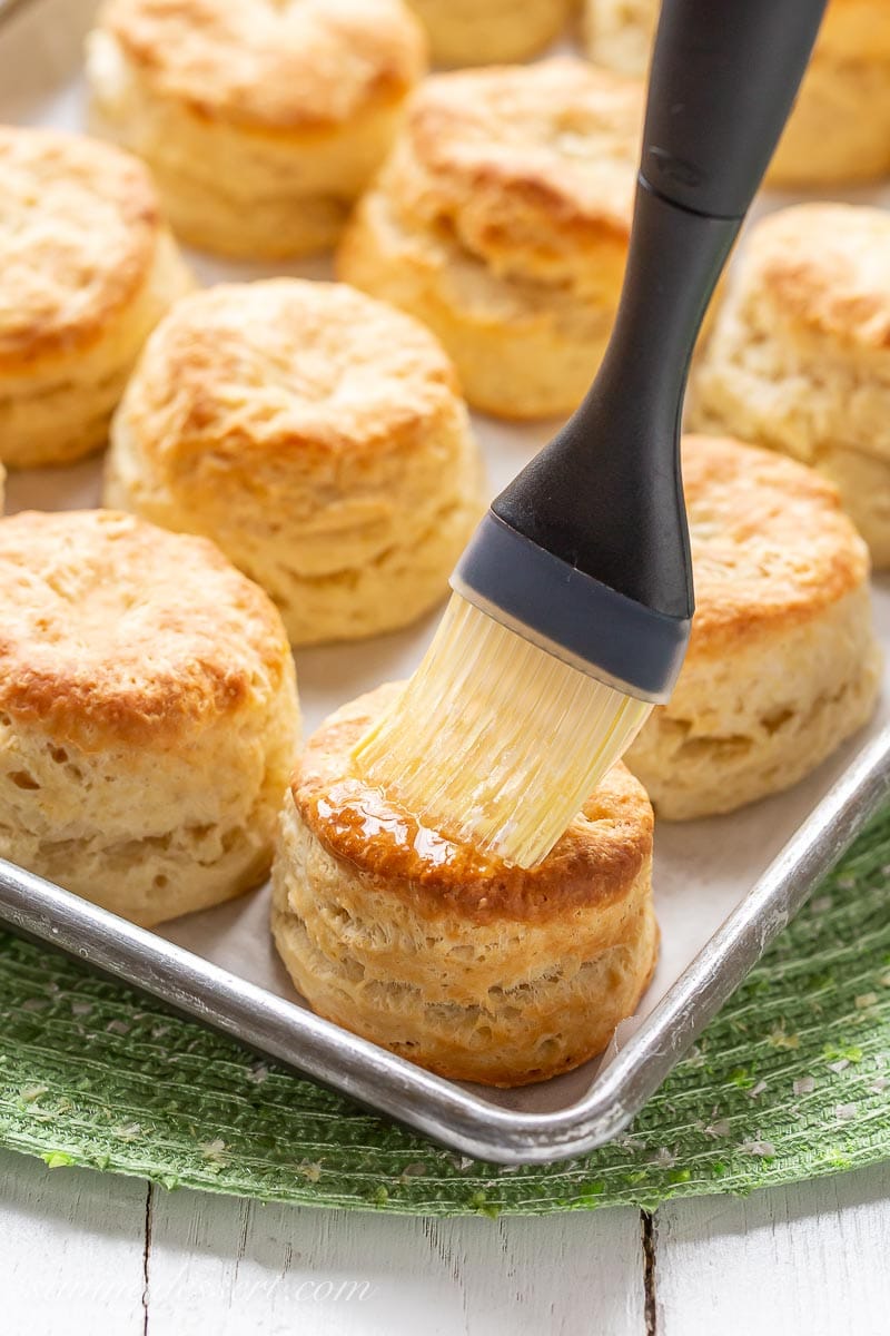 A baking pan filled with hot, golden brown buttermilk biscuits brushed with melted butter