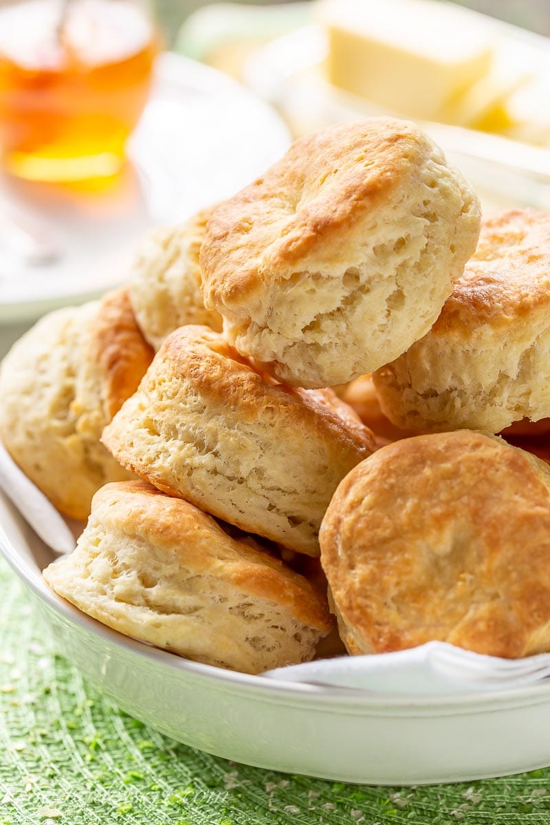 A bowl filled with fresh, hot buttermilk biscuits served with honey and butter