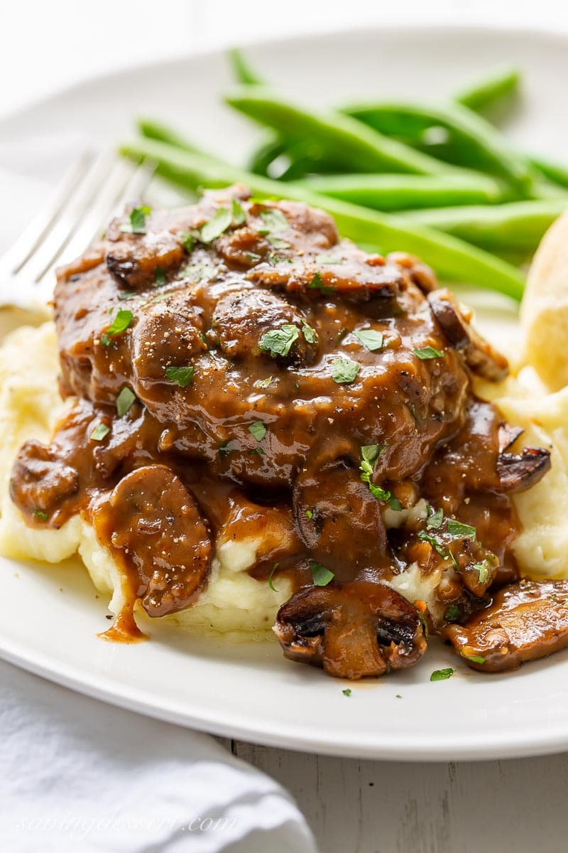 A plate with Salisbury Steak served over mashed potatoes with green beans