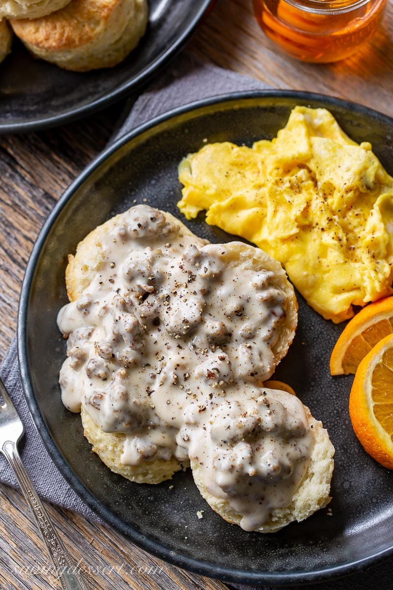 A dinner plate with biscuits and gravy with orange slices and scrambled eggs
