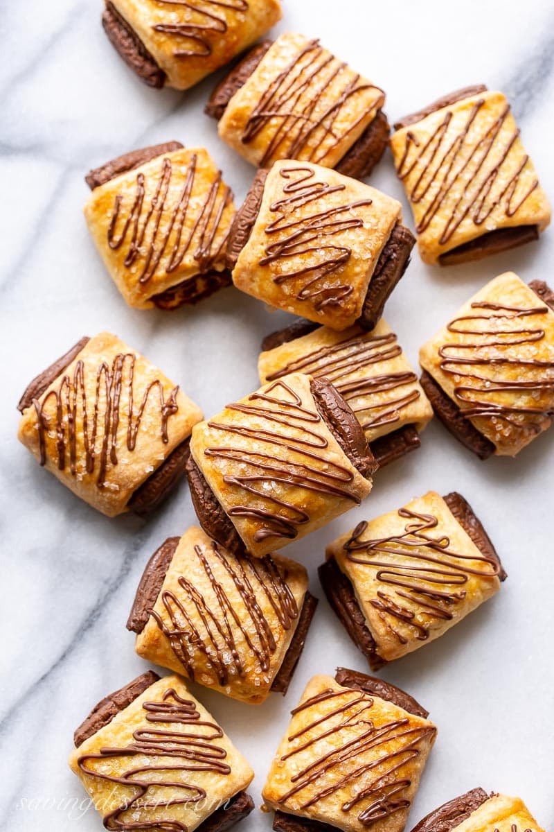 A marble table top with chocolate drizzled and filled croissant cookies scattered around