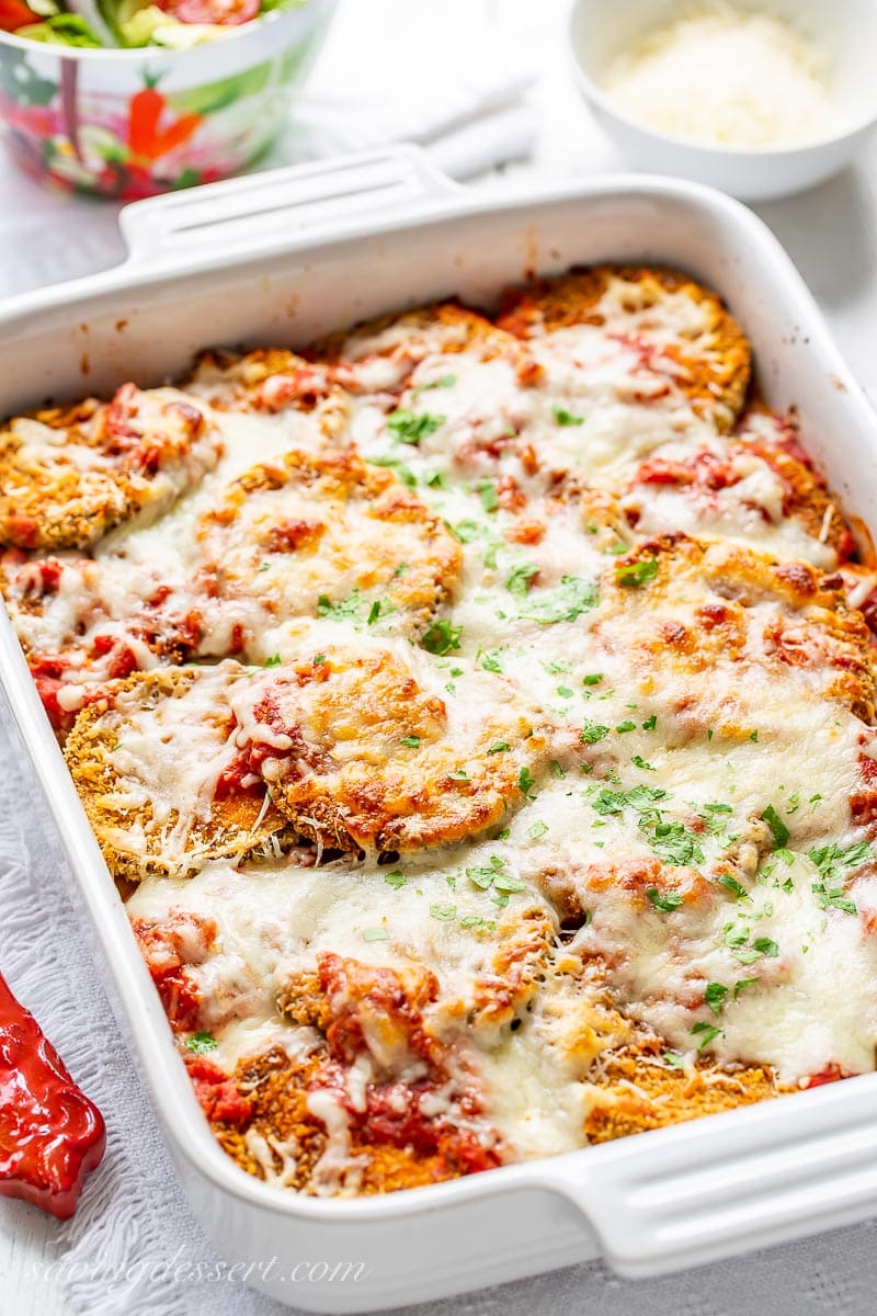 A side view of a casserole filled with eggplant Parmesan. Topped with melted cheese and parsley