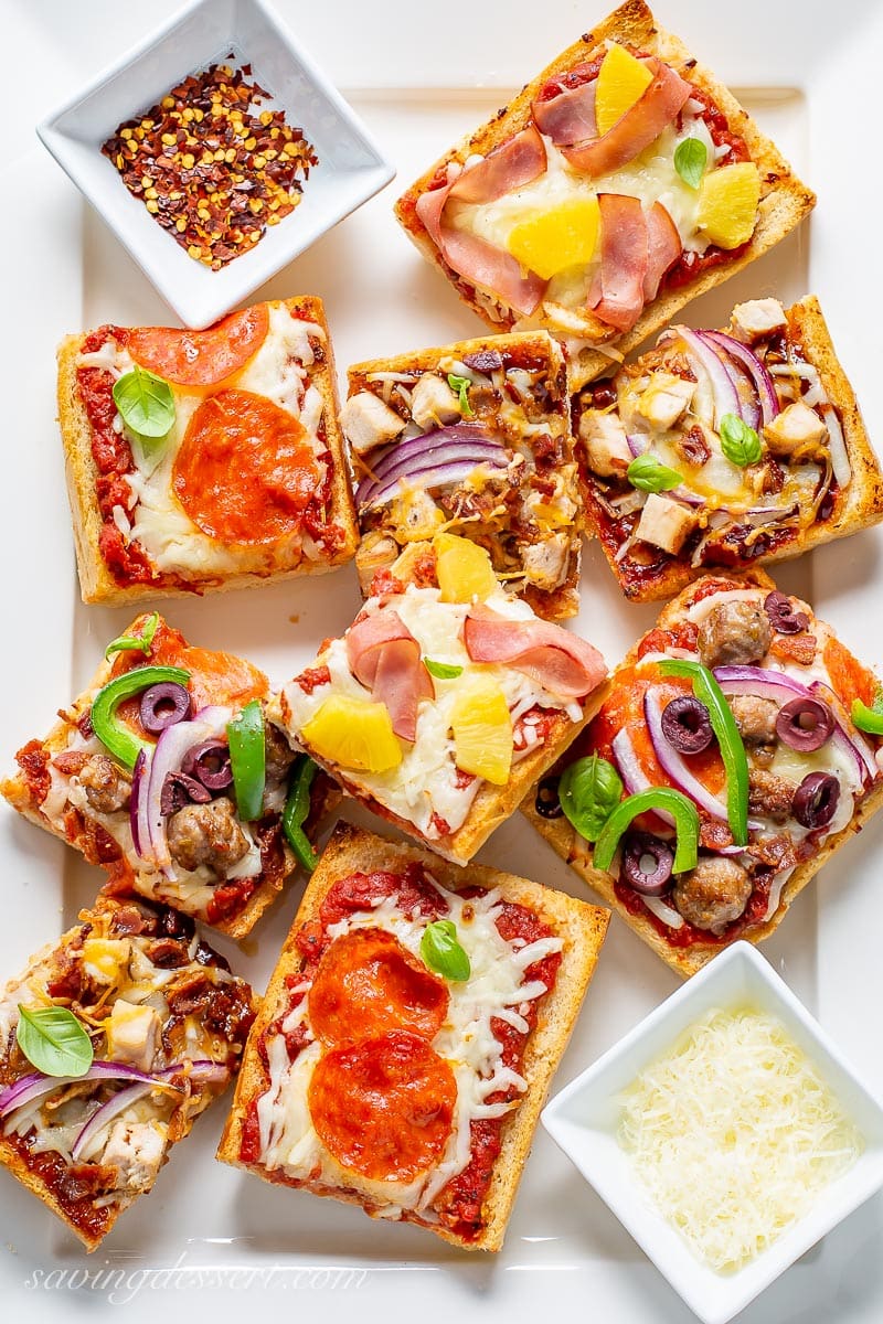 A platter of sliced French bread pizzas with a variety of topping served with red pepper flakes and fresh grated Parmesan