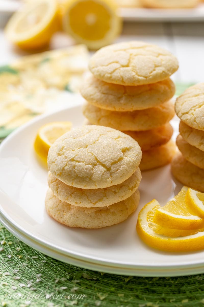 Stacks of lemon sugar cookies on a plate with lemon wedges on the side