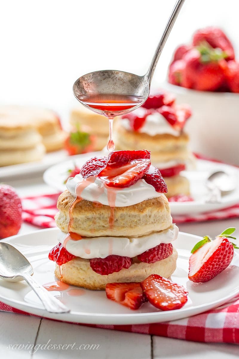 A stack of strawberry shortcake biscuits topped with whipped cream and strawberries being drizzle with juice