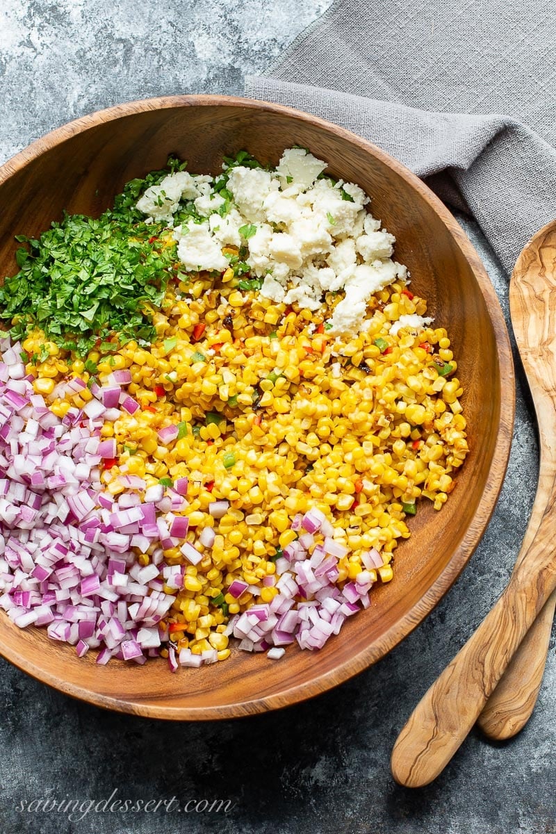 A wooden bowl with fresh corn, red onion, Queso Fresco cheese and chopped cilantro