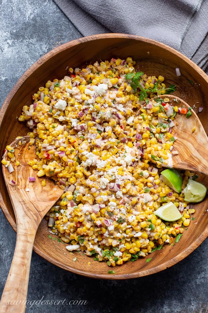 A bowl of Mexican Street Corn Salad tossed with crumbled cheese and lime wedges