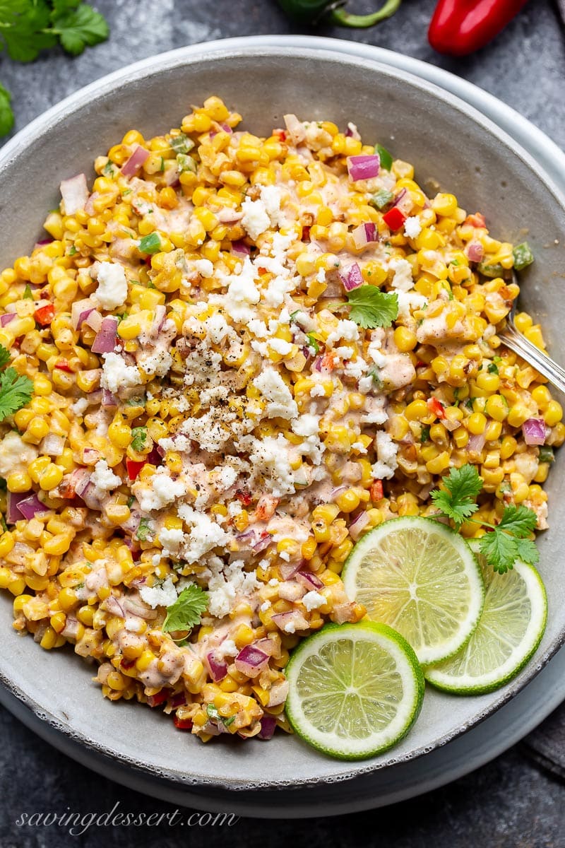 A bowl of charred corn tossed with onions, crumbled cheese, red peppers and lime juice