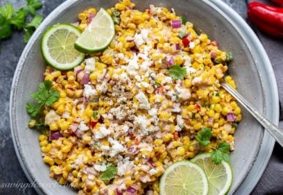 A bowl of corn salad garnished with cilantro, and fresh lime wedges