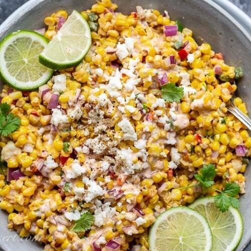 A bowl of corn salad garnished with cilantro, and fresh lime wedges