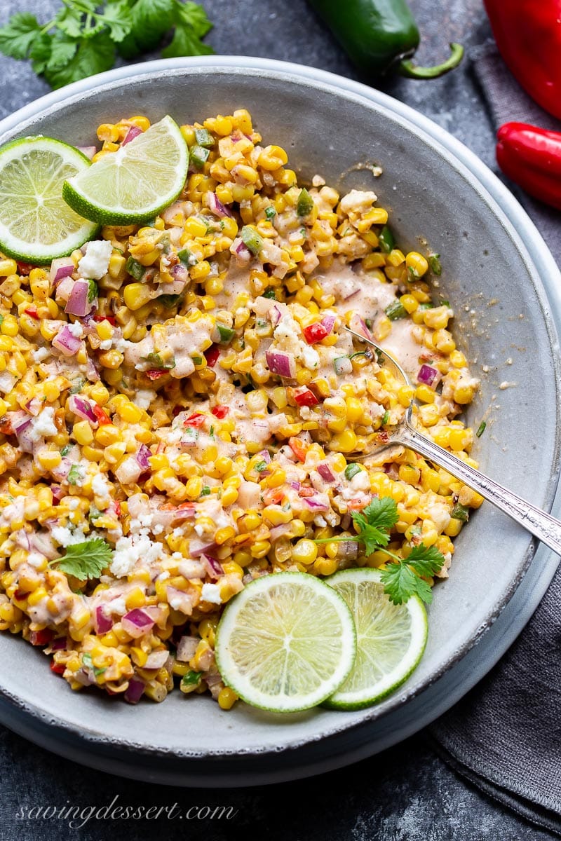 A bowl of Mexican Street Corn Salad garnished with fresh lime wedges and chopped cilantro