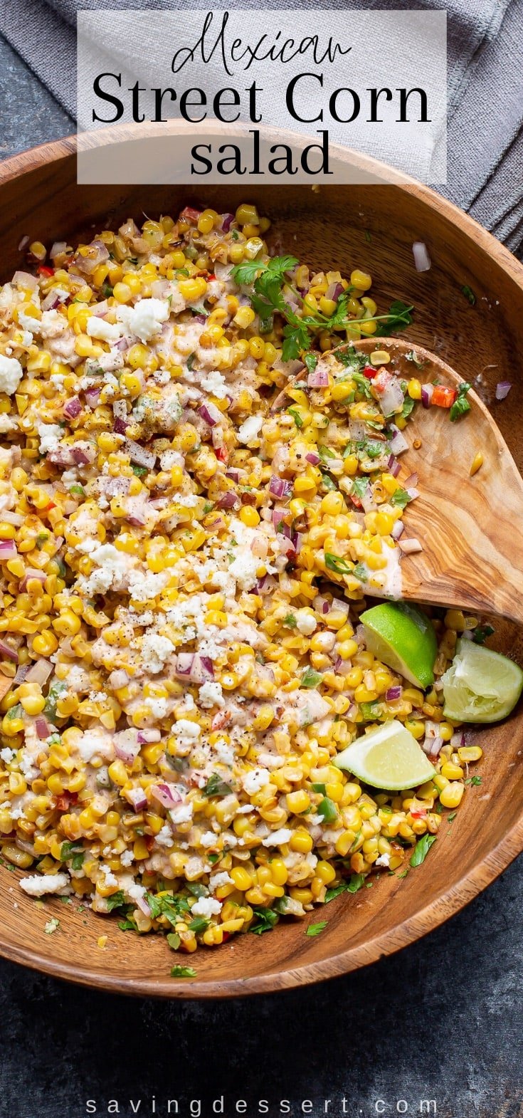 A closeup of a wooden bowl filled with a charred corn salad and a wooden spoon