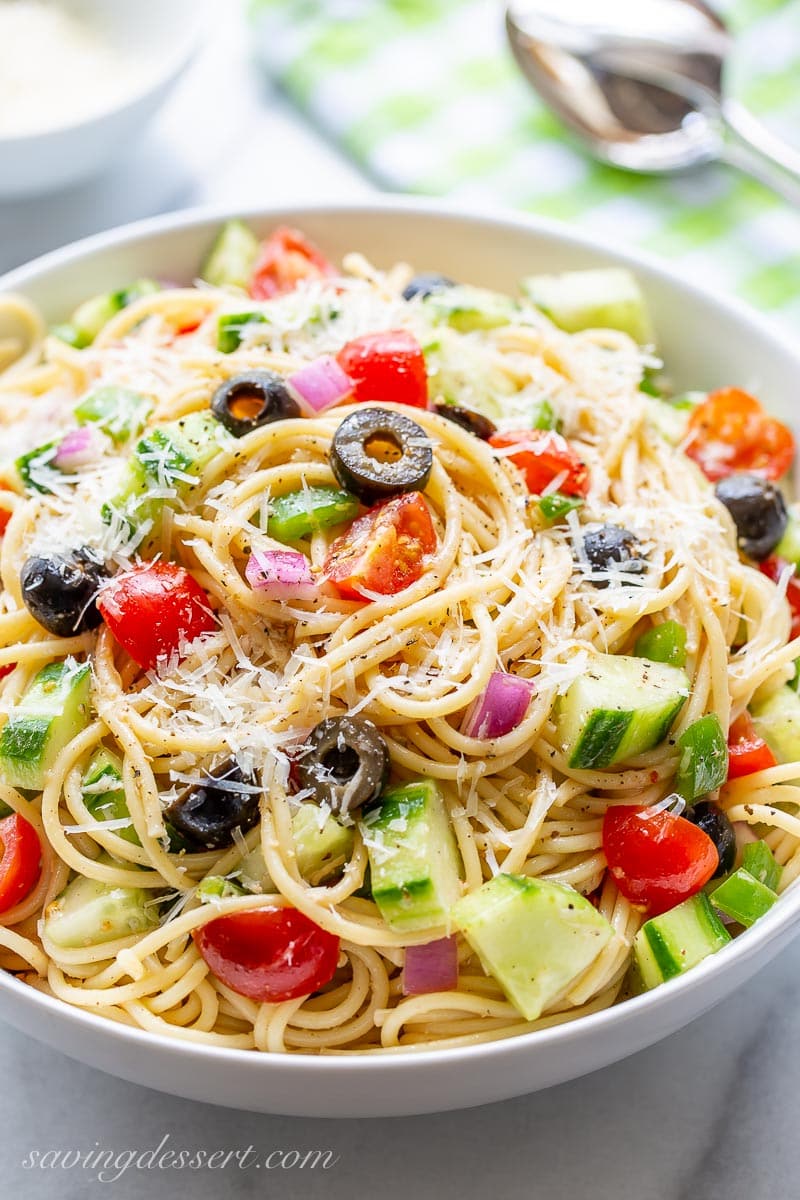 A bowl of cold spaghetti salad with tomatoes, cucumbers, black olives and green bell pepper