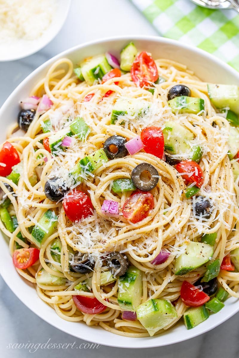 An overhead view of a bowl of cold spaghetti salad with Parmesan and vegetables