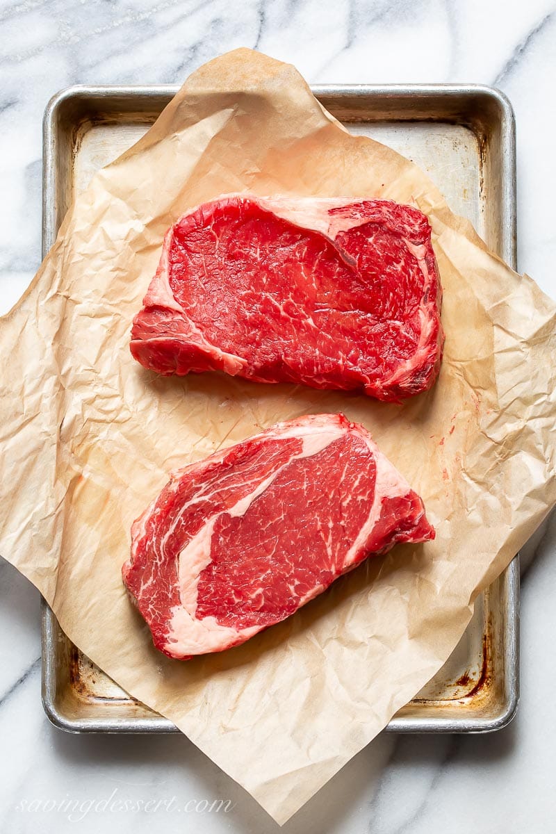 Two raw ribeye steaks on a baking pan