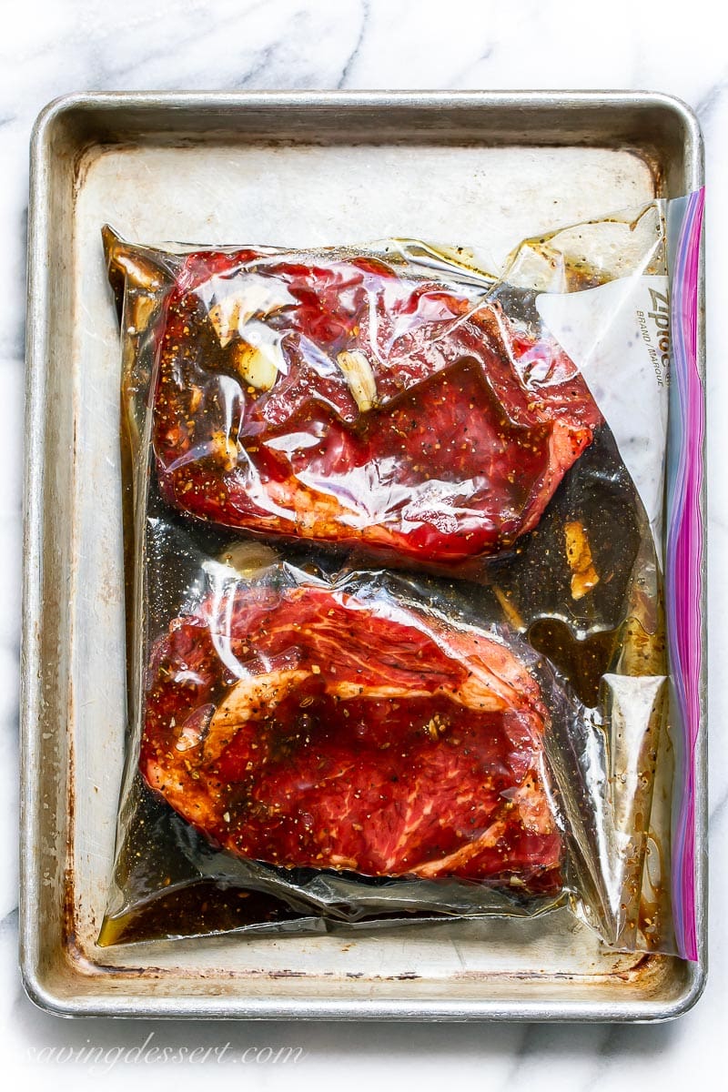 A large sealed zipper bag with two steaks in a dark marinade with cloves of garlic