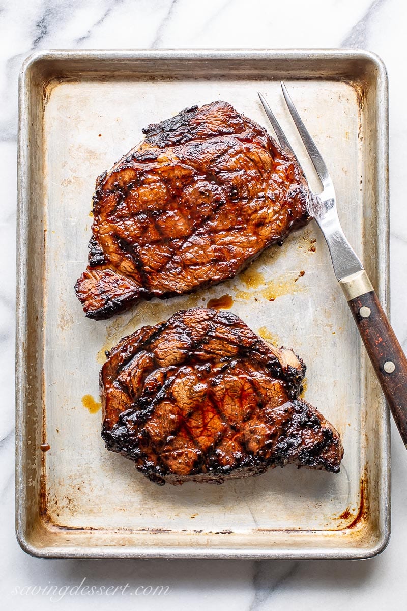 Two grilled ribeye steaks on a small baking pan with a large fork