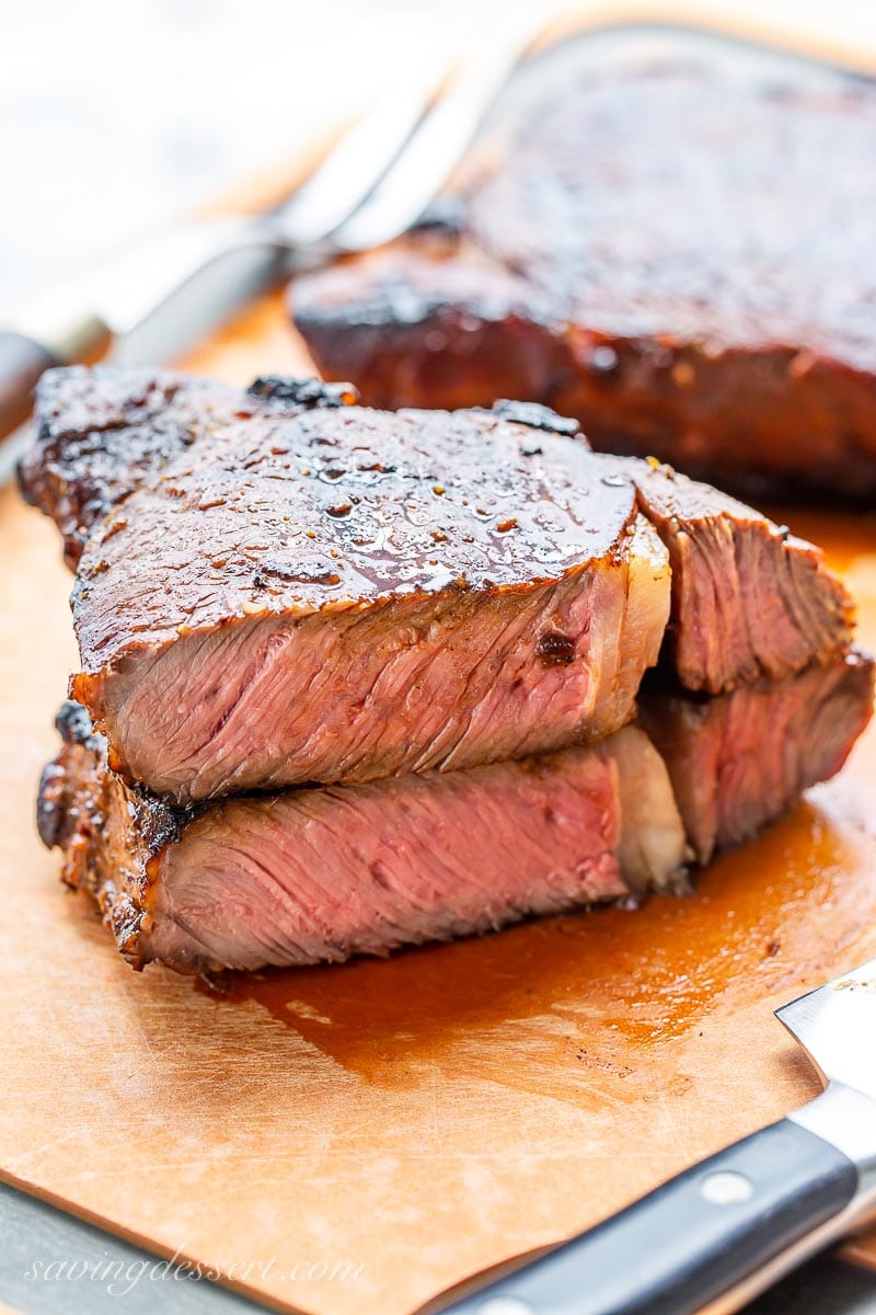 A grilled ribeye steak cut in half and stacked on a cutting board, to show the pale pink interior and juicy texture