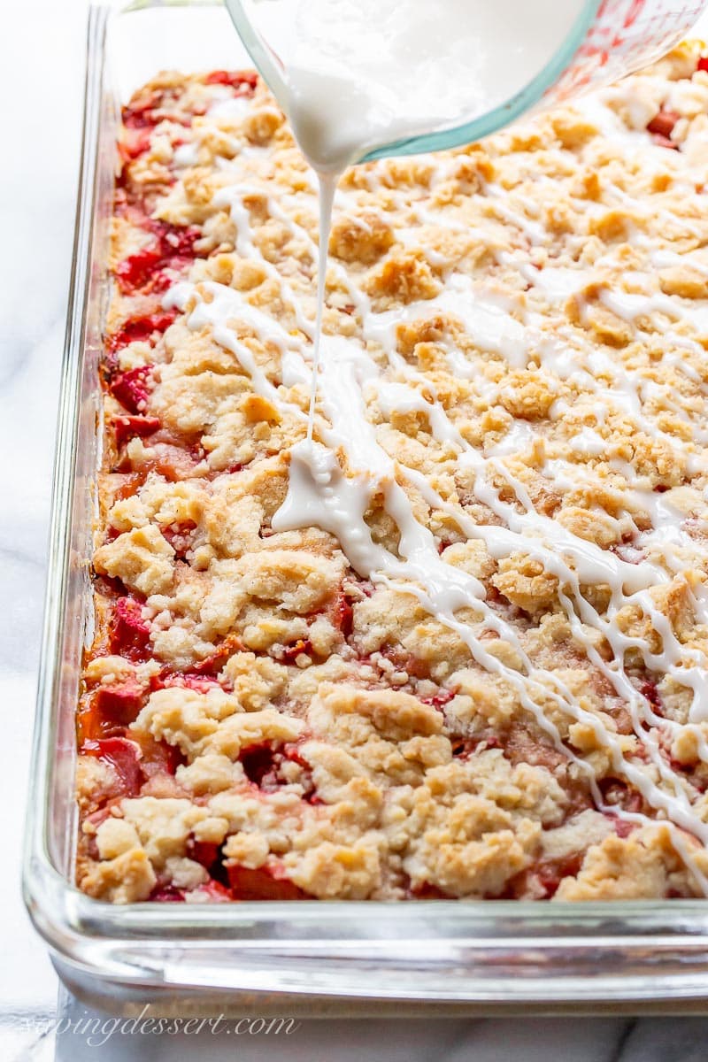 A pan of baked strawberry rhubarb crumble bars being drizzle with icing
