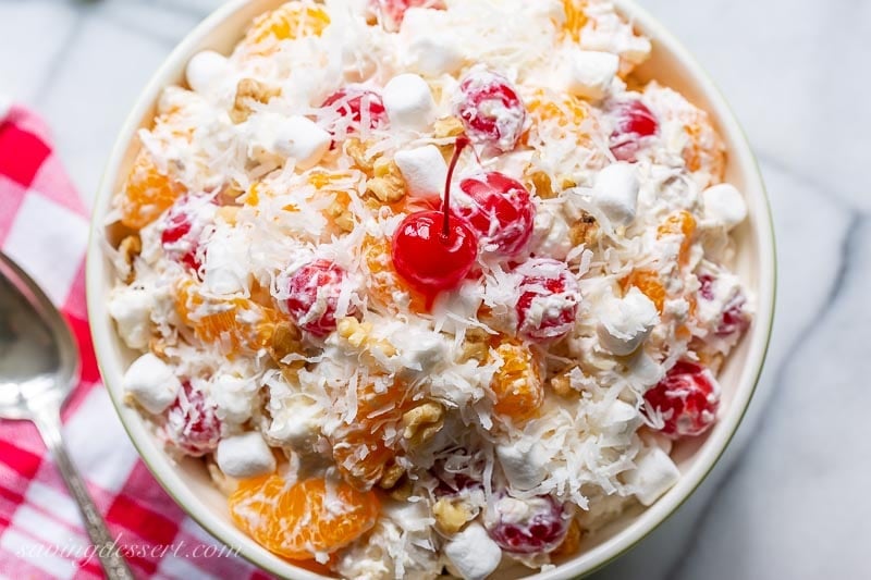 A bowl of fruit topped with a bright red cherry and shredded coconut in a creamy sour cream dressing