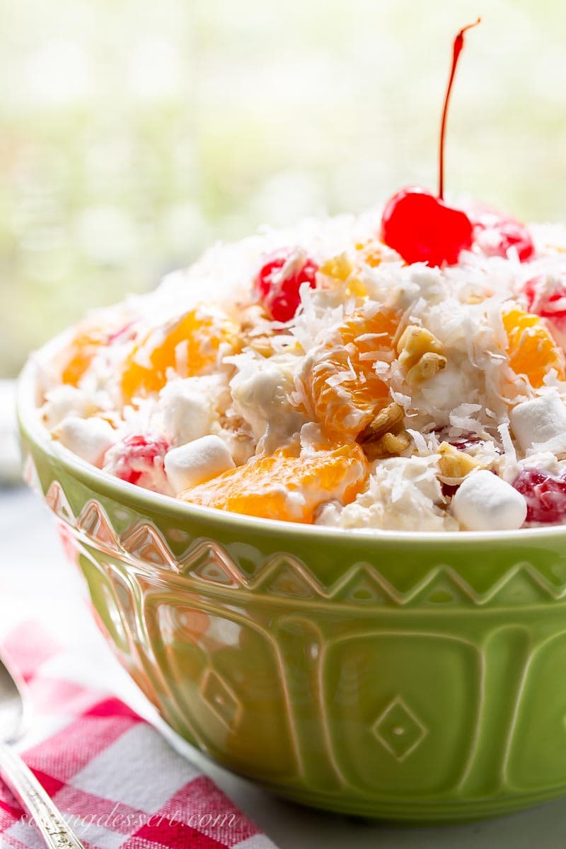 A side view of a green bowl filled with Ambrosia fruit salad topped with a cherry