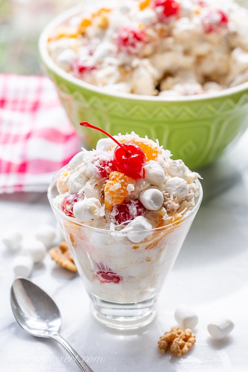 A small glass filled with a fruit salad with marshmallows, mandarin oranges and cherries