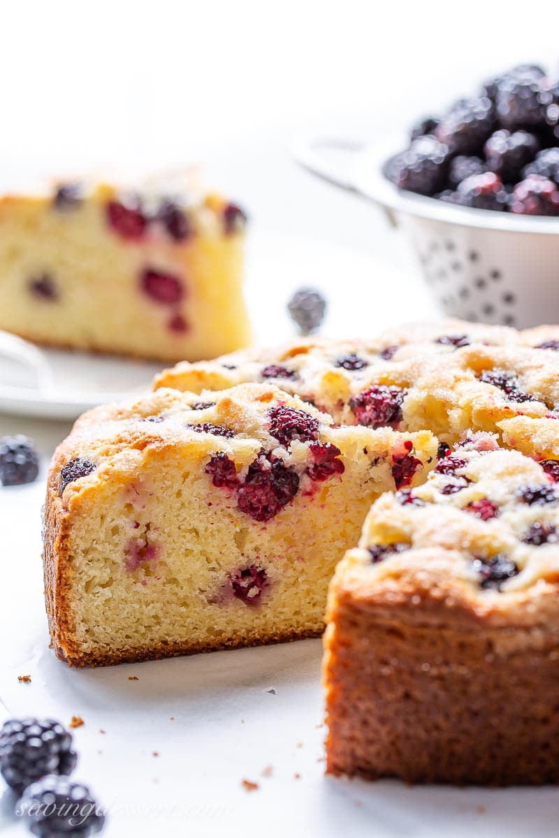 A side view of a sliced cake with fresh blackberries and more in the background