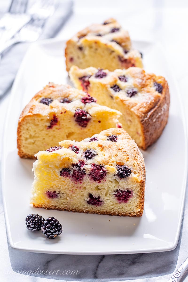 A platter with four slices of cake baked with fresh blackberries on top