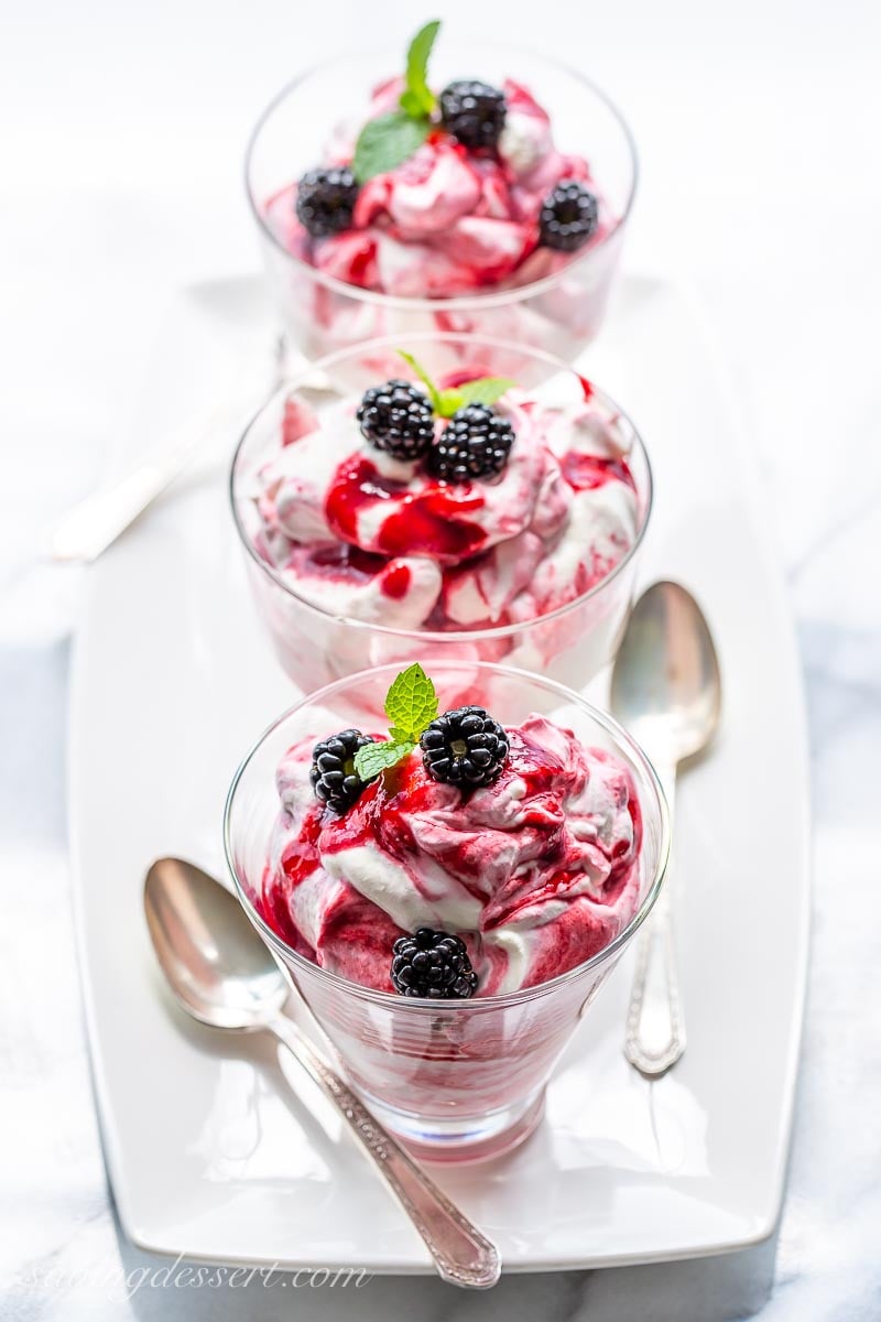 An overhead view of three Blackberry Fool desserts on a platter with spoons