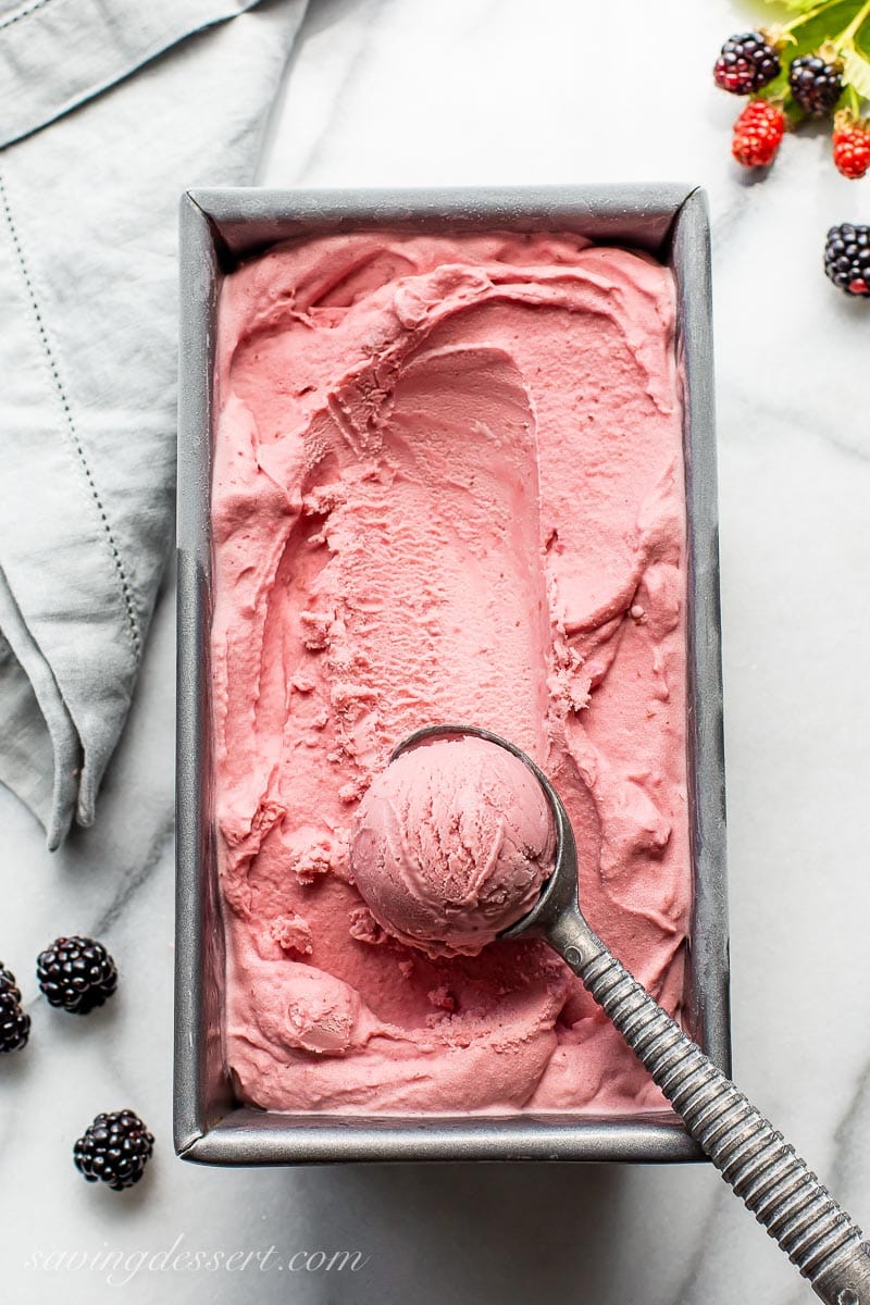 A small loaf pan filled with pink hued ice cream with a scoop