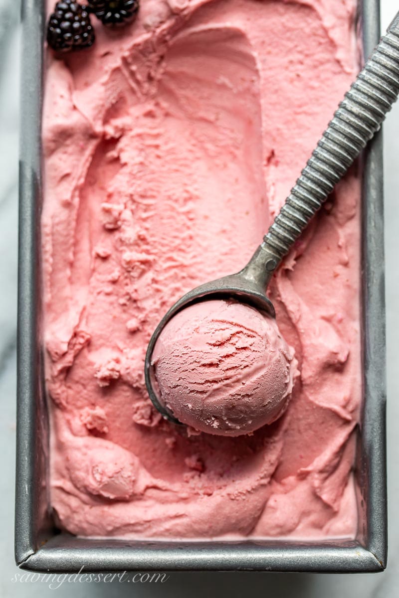 A close up photo of a pan of blackberry ice cream with a scoop