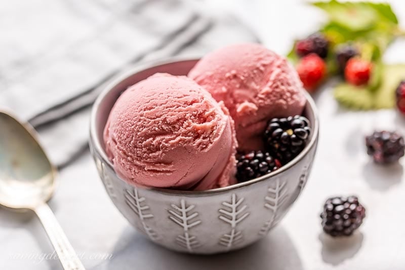A small gray bowl with three scoops of frozen pink dessert with blackberries