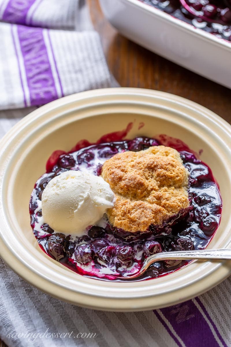 A bowl of blueberry cobbler and a scoop of vanilla ice cream with a spoon