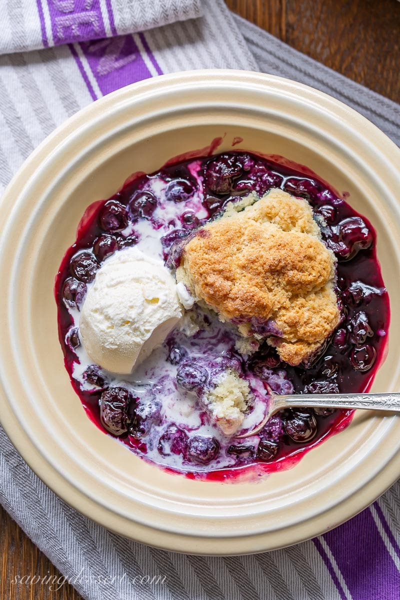 An overhead view of a bowl of cobbler with blueberries and ice cream